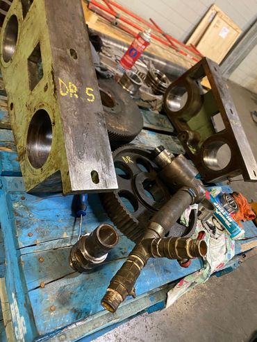 Industrial metal parts and gears laid out on a blue wooden pallet in a workshop.