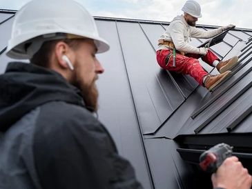 Two construction workers installing metal roofing on a house.