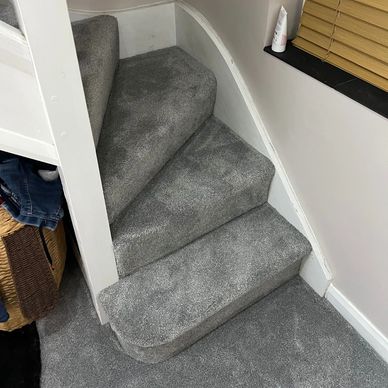 Gray carpeted stairs with a small landing area and beige walls.