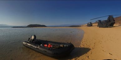 military zodiac on the beach with two HH-47 in the backround