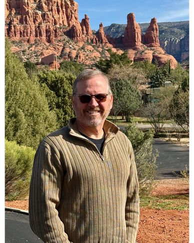 Man smiling in sunglasses with red rock formations in background.