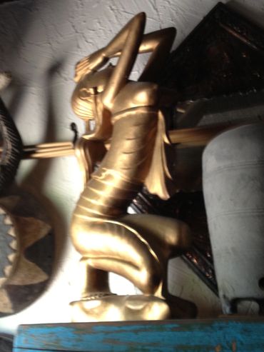 Golden statue of a person kneeling with hands on head, surrounded by artifacts.