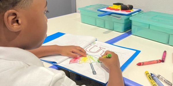 Child coloring a drawing of an umbrella at a desk.