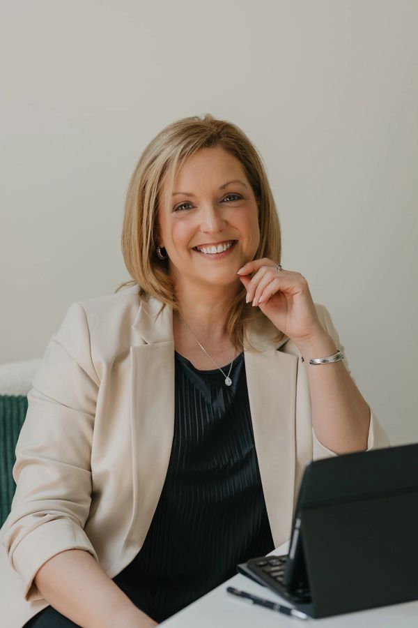 Smiling woman in business attire sitting at desk with tablet.