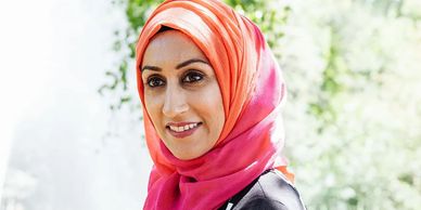 Sam headshot at P&G with pink scarf and green trees behind