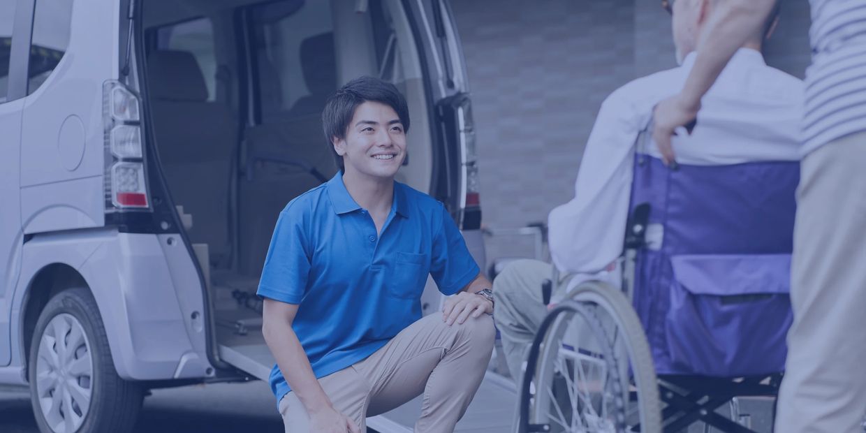A caregiver helps a person in a wheelchair near a vehicle.