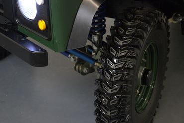 Close-up of a rugged off-road tire and suspension on a green vehicle.