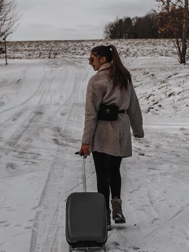 Woman walking on snowy path pulling a suitcase, dressed warmly.