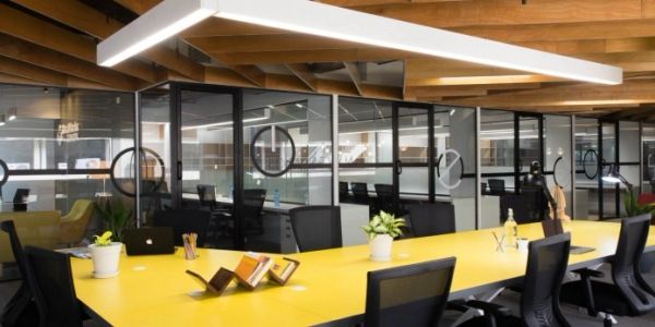 Modern office with a bright yellow table and glass partitions.
