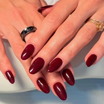 Hands with dark red glossy almond-shaped nails and rings.