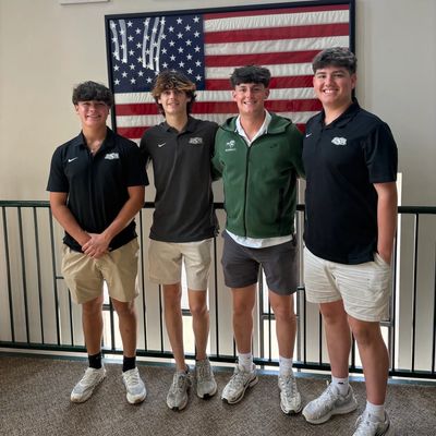 Four young men standing in front of an American flag, smiling.