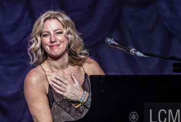 Woman smiling with hand on chest near piano.