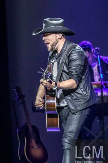 Musician in a cowboy hat passionately playing guitar on stage.