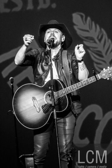 Black-and-white photo of a male musician singing with a guitar on stage.