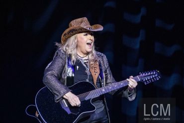 Woman in cowboy hat playing a black guitar on stage.