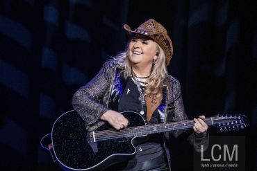 Musician in a cowboy hat playing a black acoustic guitar on stage.