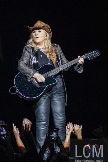 Female musician playing guitar on stage wearing a cowboy hat.