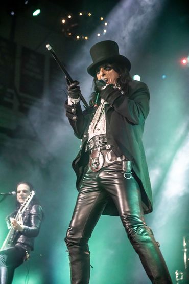 Rock musician in theatrical outfit with top hat and cane on stage.