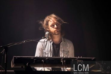 Man playing keyboard on stage with thoughtful expression.