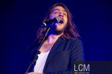 Man singing passionately into microphone on stage.