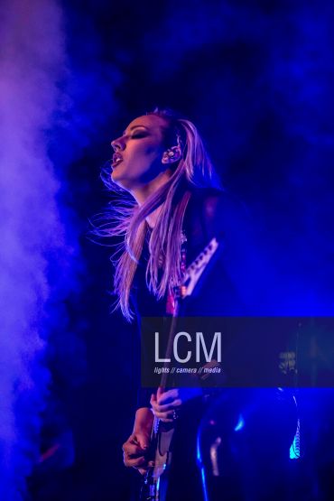 Guitarist performing passionately on stage with blue lighting and smoke.