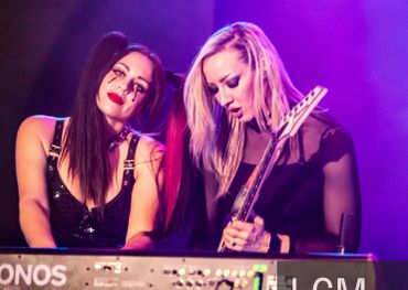 Two women passionately playing keyboard and guitar on stage.