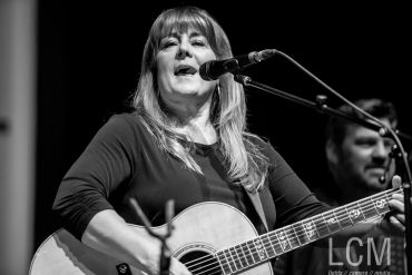 Black and white photo of a woman singing and playing guitar on stage.