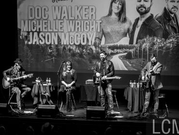 Black and white image of a live musical performance with four artists on stage.