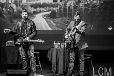 Two musicians performing on stage, one playing guitar and the other singing.