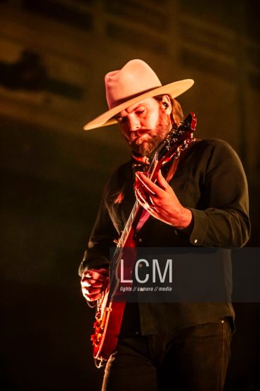 Musician playing guitar wearing a wide-brimmed hat.