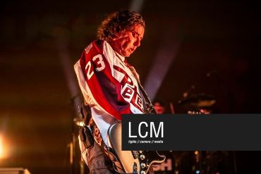 Musician playing guitar on stage in intense lighting.