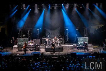 Rock band performing on stage with blue spotlights and audience.