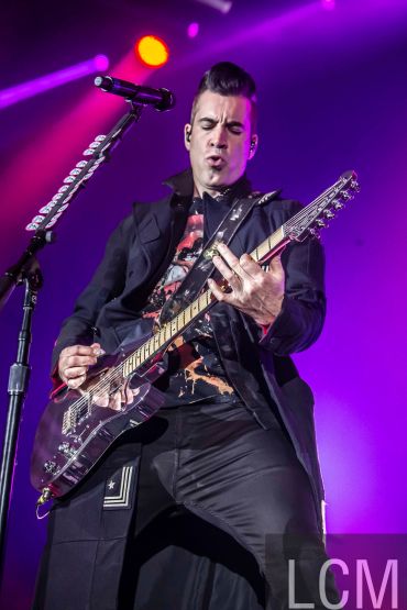 Guitarist passionately playing on stage under vibrant purple and orange lights.