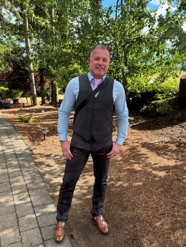 Man in formal attire posing outdoors on a sunny day.