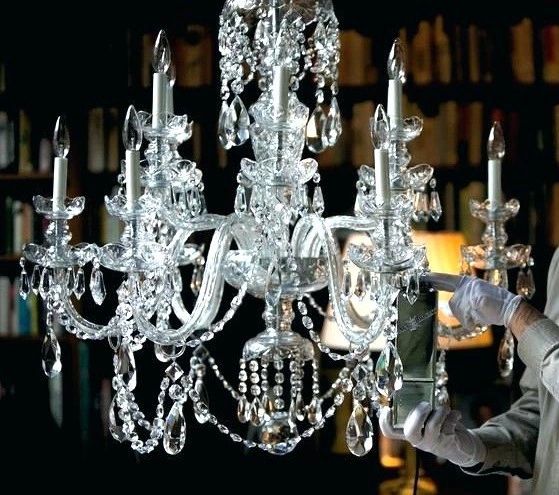 Person cleaning a crystal chandelier with a spray bottle.