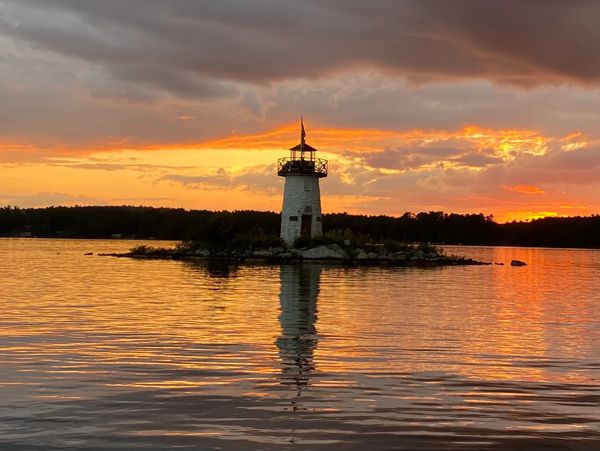 Lighthouse silhouetted against a vibrant sunset over calm water.