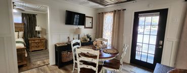 Cozy dining area with rustic white chairs and wooden table near a glass-paneled door.
