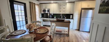 Cozy kitchen and dining area with rustic white cabinets and wooden flooring.