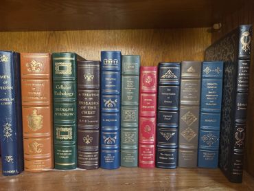 A row of classic medical books with ornate bindings on a wooden shelf.
