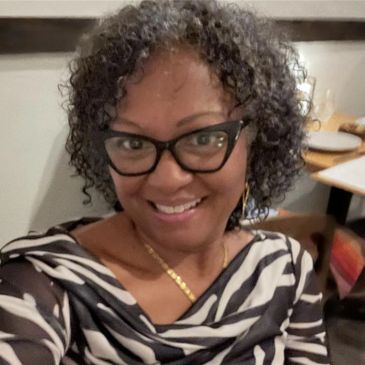 Smiling woman with curly hair and glasses wearing a striped top.