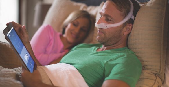 Man using a CPAP machine while lying in bed with a woman.