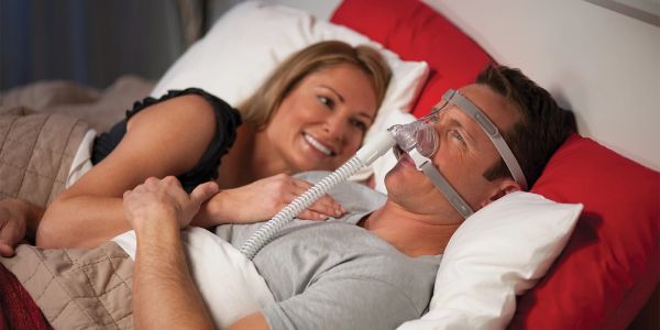 Couple in bed, man using CPAP mask.