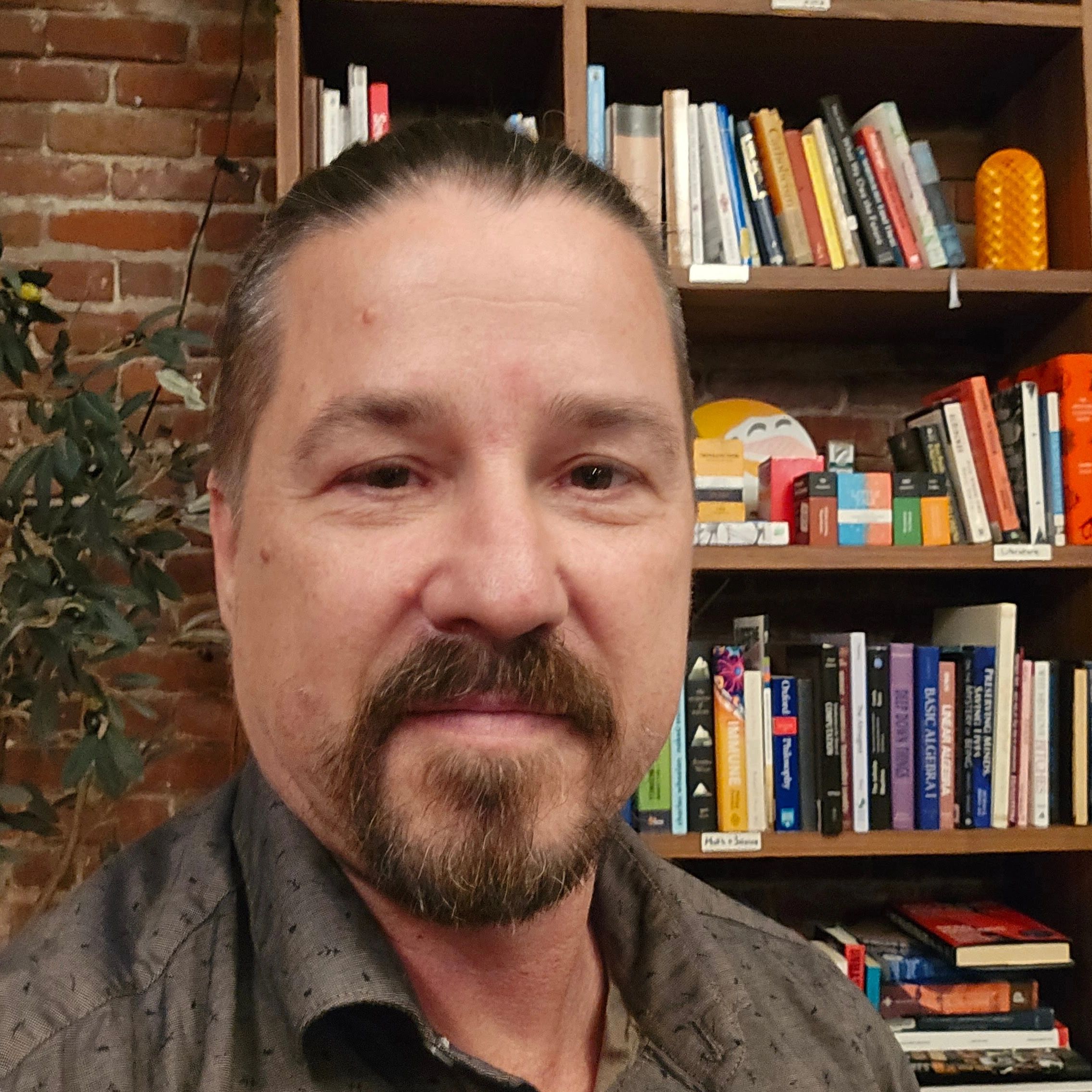 Brian Oney infront of a wall of books and bricks.