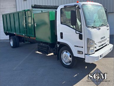White and green Isuzu flatbed truck parked outside a building.