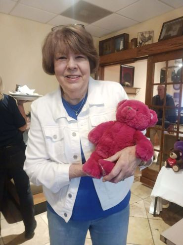 Woman smiling while holding a bright pink teddy bear indoors.