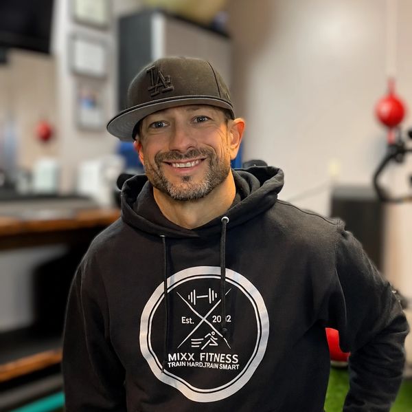 Man smiling in a gym wearing a black hoodie and cap.
