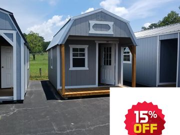 Small gray and white storage shed with a front porch on a paved lot.