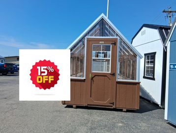Small brown greenhouse with glass panels under a clear blue sky.