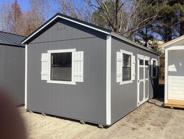 Gray storage shed with white trim and shutters, situated outdoors.