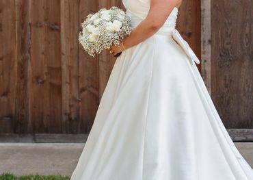 Bride in a white wedding dress holding a bouquet, standing against a wooden backdrop.